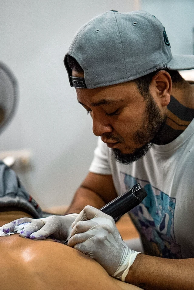 El artista de FENIX tatuando con guantes, concentrado en el trabajo